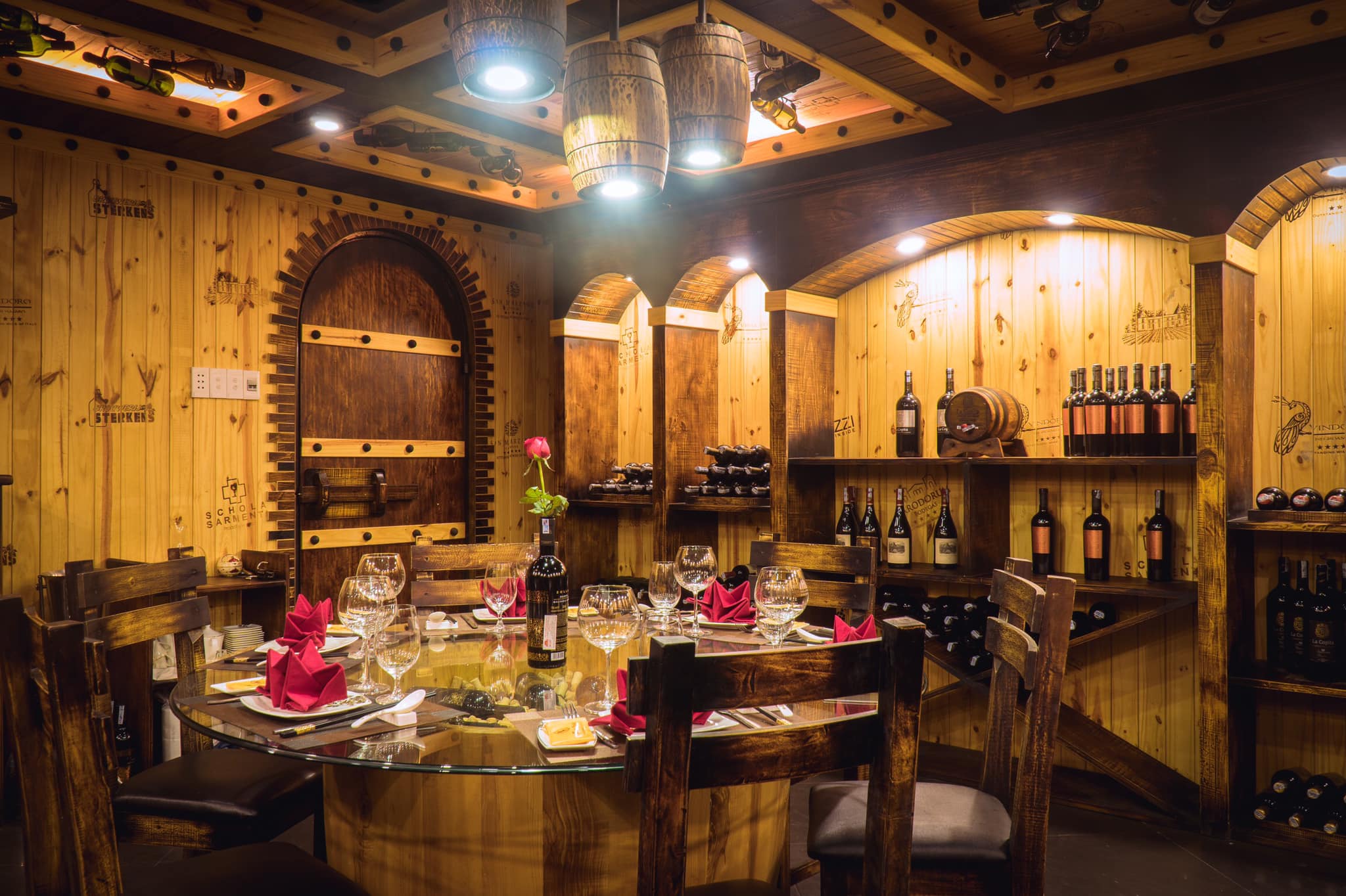 Hầm rượu vang phong cách cổ điển với bàn ăn tròn, nến thủy tinh, chai rượu và trang trí sang trọng.