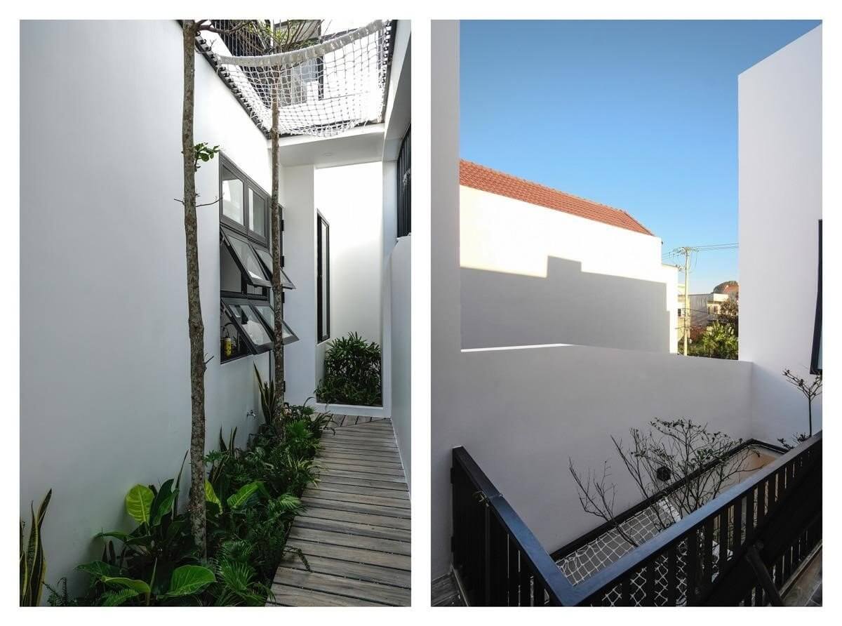 Lối đi lát ván gỗ ngoài trời với cây xanh và tường trắng, thiết kế hiện đại và thoáng đãng.