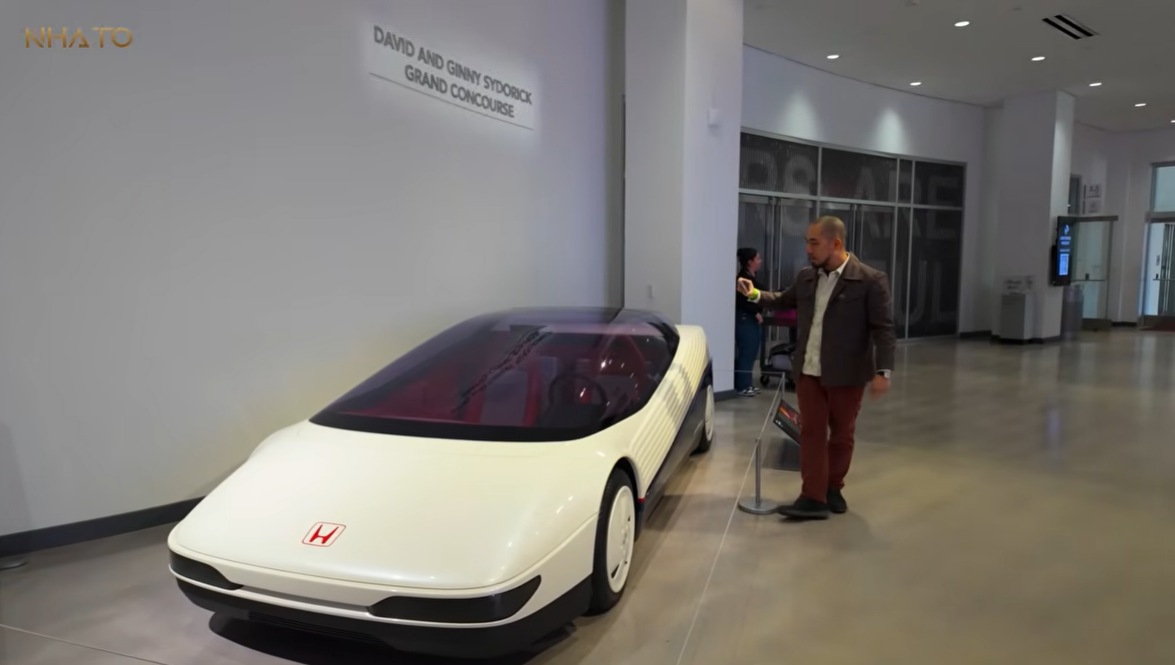 honda-1984 Xe ý tưởng Honda cửa kính tại bảo tàng, nam du khách đang giơ điện thoại chụp hình, không gian nội thất hiện đại.