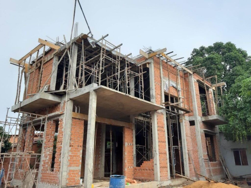 Công trình xây dựng nhà hai tầng bằng gạch đỏ đang hoàn thiện với giàn giáo bao quanh.