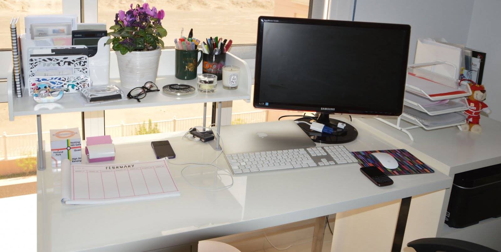 Bàn làm việc gọn gàng với máy tính, tài liệu và cây trang trí, ánh sáng tự nhiên từ cửa sổ lớn.