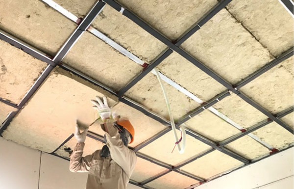 huong-dan-cach-am-tran-va-san Công nhân lắp đặt trần chống cháy với vật liệu cách nhiệt, đội mũ bảo hộ và găng tay an toàn.