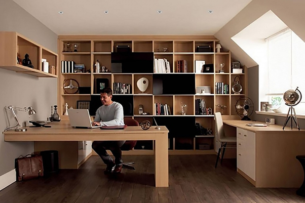 Người đàn ông làm việc tại bàn trong văn phòng tại gia với kệ sách lớn và ánh sáng tự nhiên.