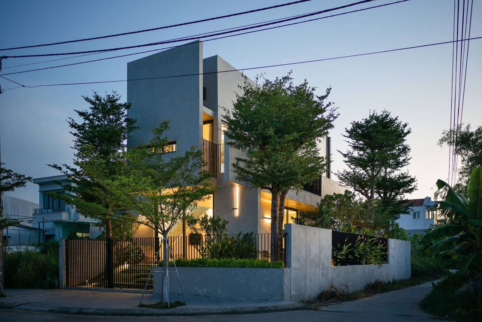 Nhà hiện đại với thiết kế tối giản, ánh sáng ban đêm, cây xanh bao quanh ở khu dân cư yên tĩnh.