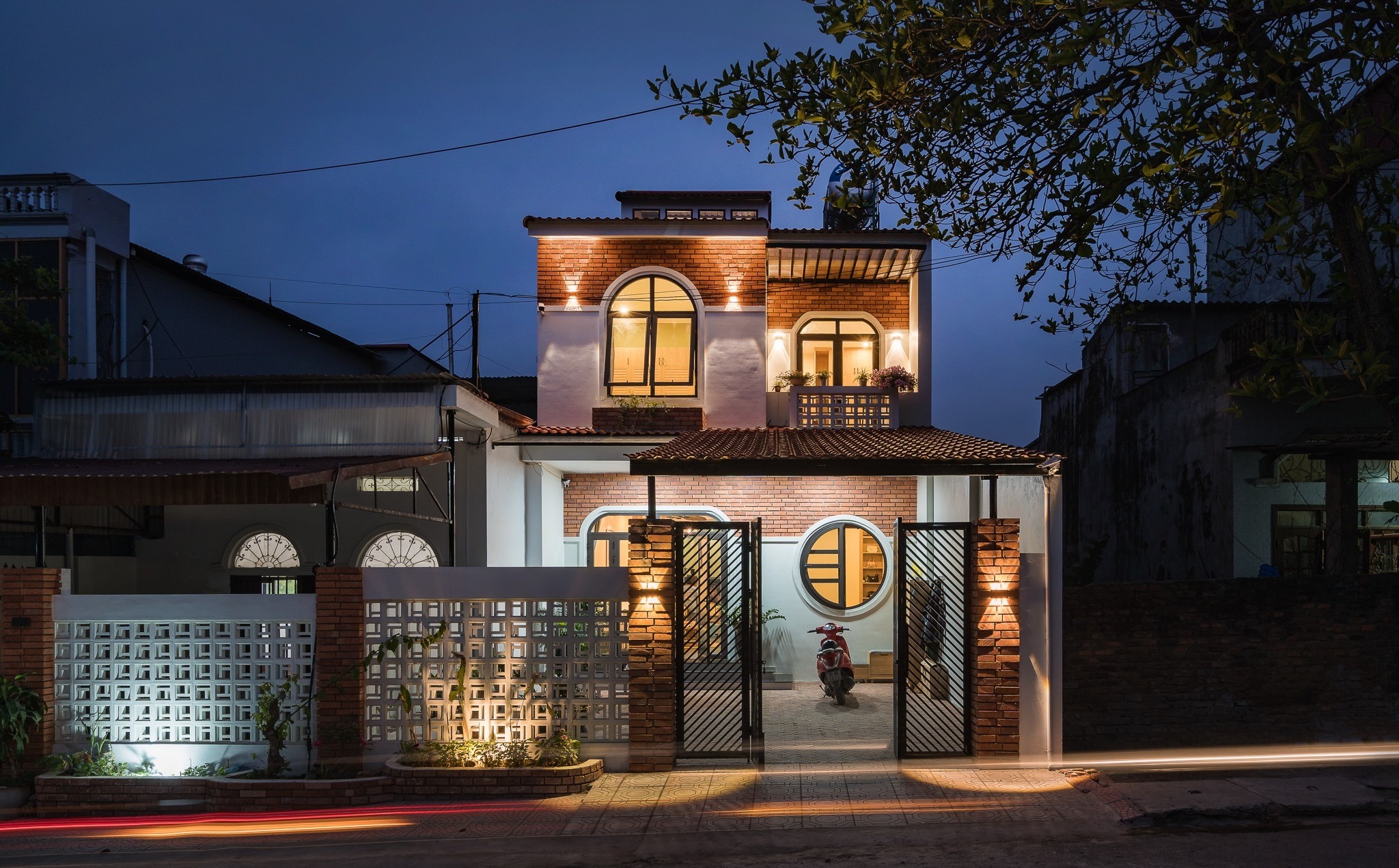 Ngôi nhà hai tầng phong cách hiện đại với ánh sáng ấm áp vào ban đêm, nổi bật giữa khu phố.