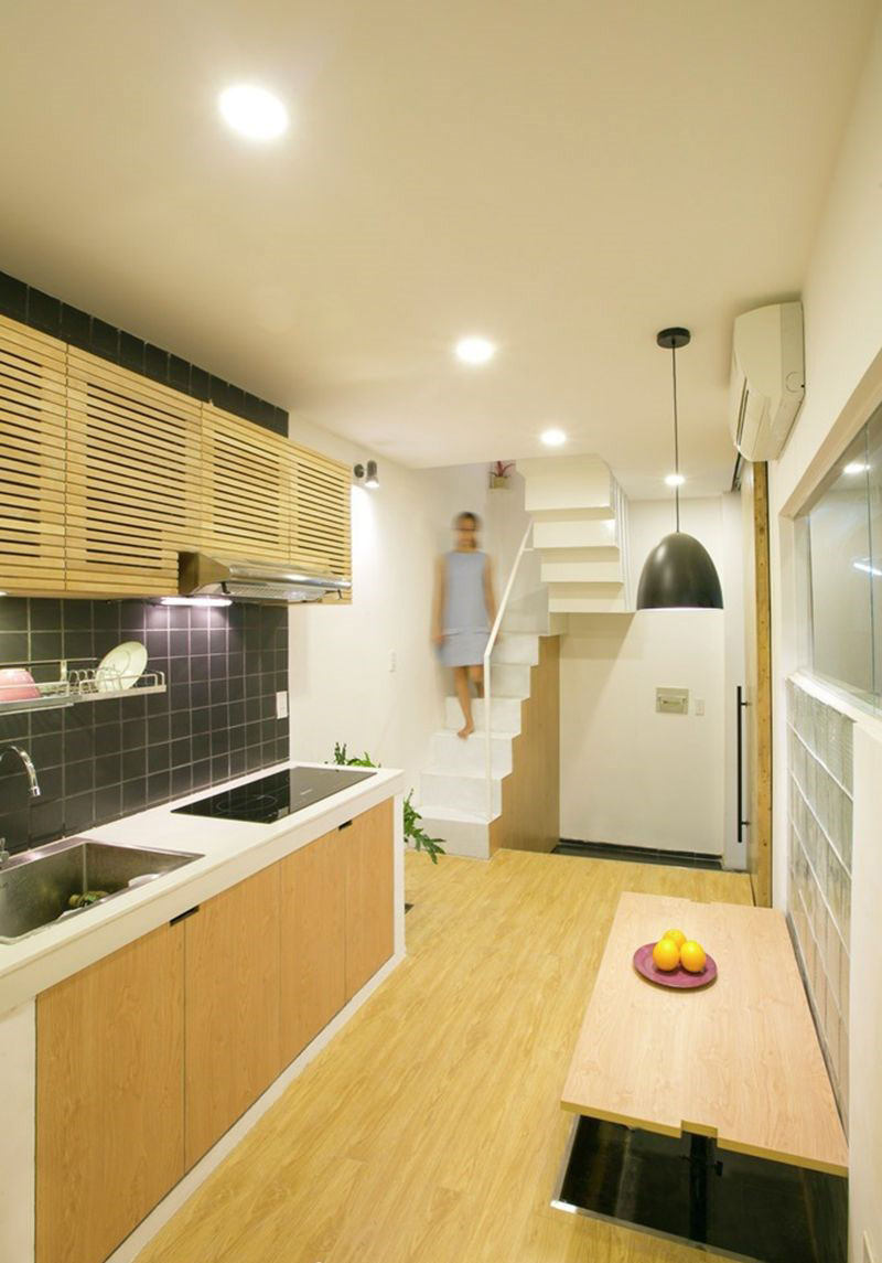 Phòng bếp hiện đại với tủ gỗ, bàn ăn gọn gàng và cầu thang trắng sáng, người phụ nữ đang bước xuống.