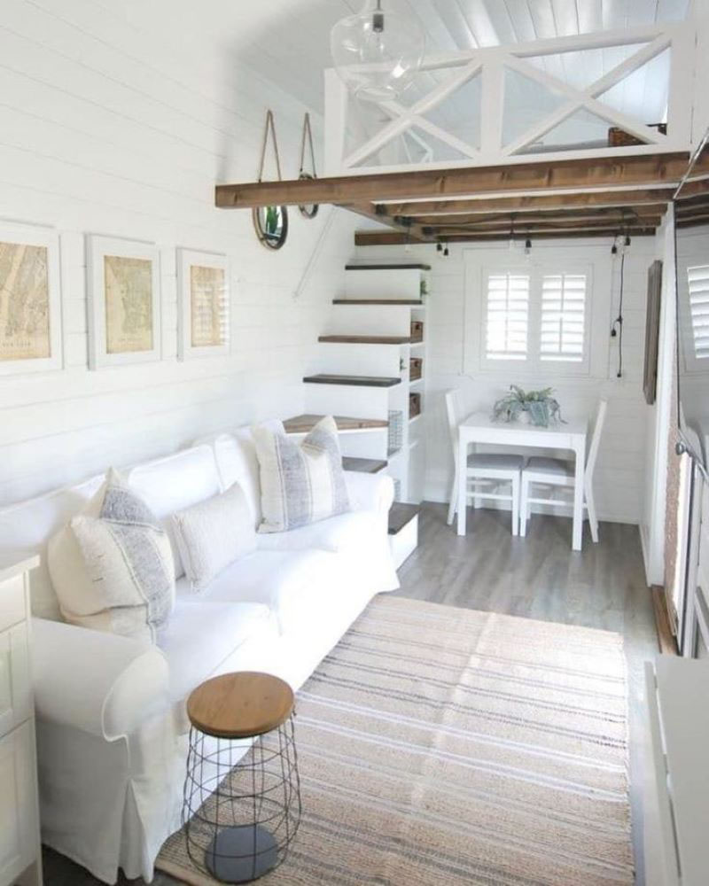 Phòng khách nhỏ gọn với ghế sofa trắng và cầu thang gỗ dẫn lên gác xép, nội thất tối giản và hiện đại.