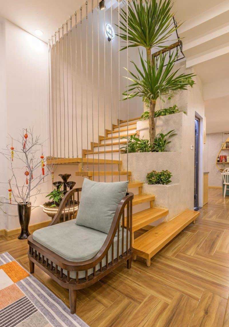Cầu thang gỗ hiện đại với cây xanh, ghế đệm thoải mái và sàn gỗ trong phòng khách ấm cúng.