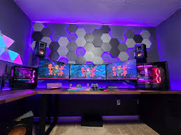 Bộ máy tính chơi game với ba màn hình, đèn LED tím và tường trang trí 3D trong không gian tối.