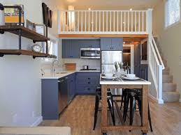 Nhà bếp nhỏ gọn hiện đại với tủ màu xám, bàn ăn bằng gỗ, ghế màu đen, và gác lửng trắng sáng.