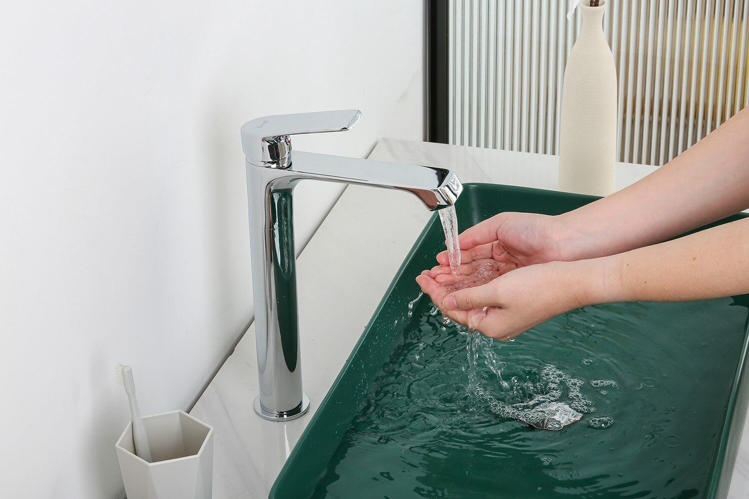 Người rửa tay dưới vòi nước chảy trong bồn rửa màu xanh lá cây, vòi bằng kim loại sáng bóng.