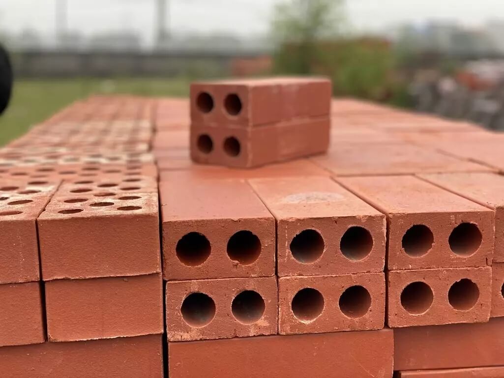 Đống gạch đỏ xếp chồng, với gạch trên cùng nổi bật trong ánh sáng tự nhiên ngoài trời.