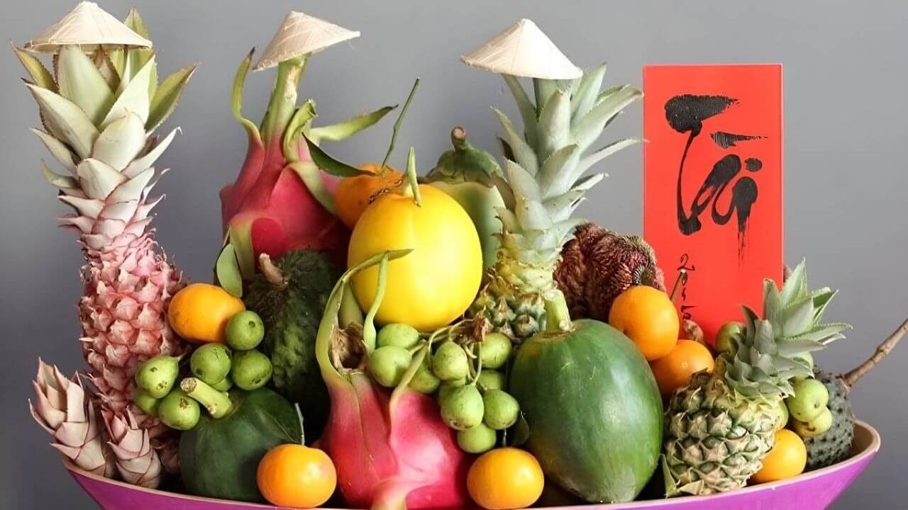 Mâm ngũ quả Tết với trái cây nhiệt đới và nón lá, thẻ thư pháp đỏ trang trí truyền thống.