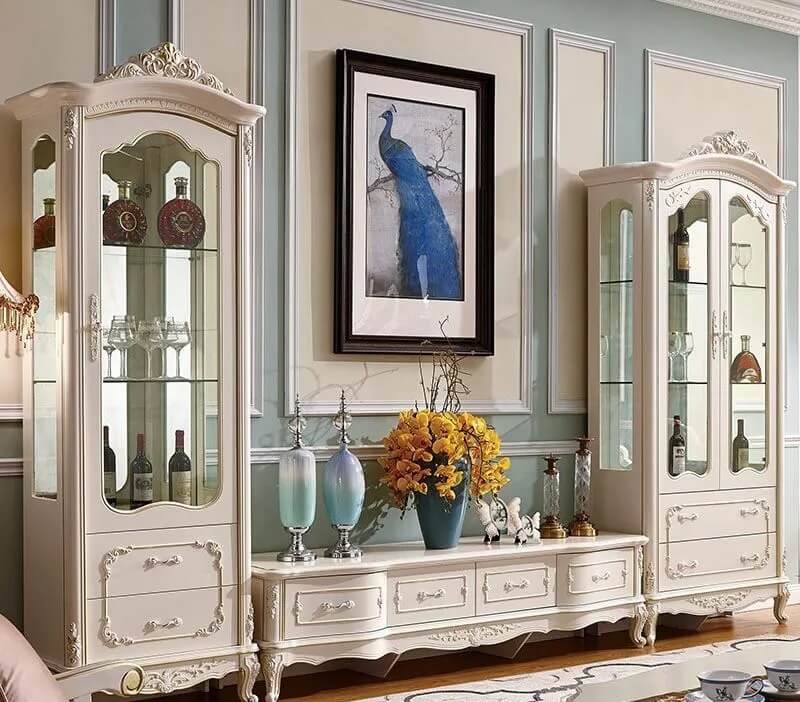 Tủ trưng bày cổ điển màu trắng, tranh chim công xanh, lọ hoa trang trí, phòng khách sang trọng.