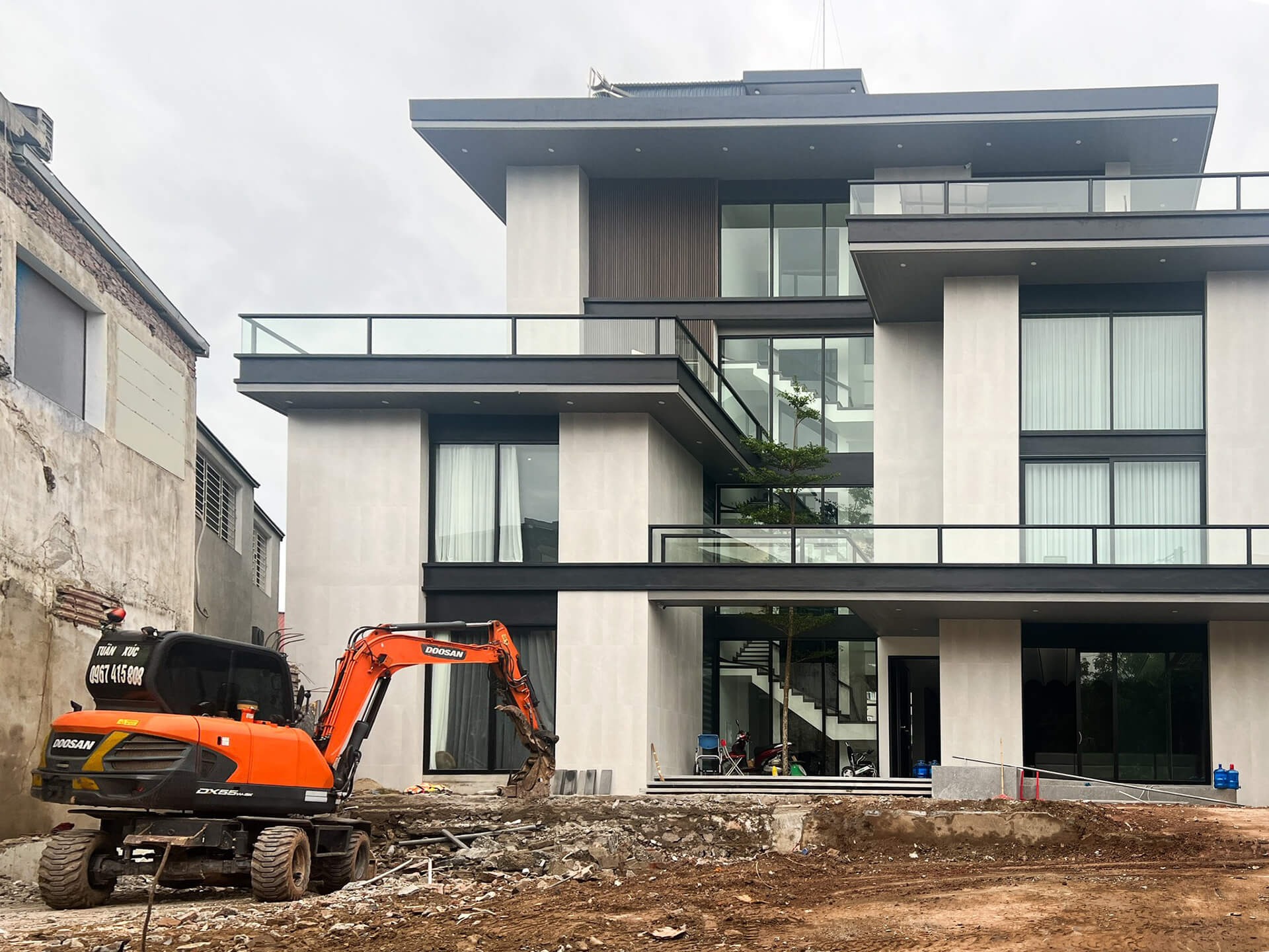 Công trình biệt thự hiện đại với máy xúc đất đang làm việc phía trước tòa nhà.
