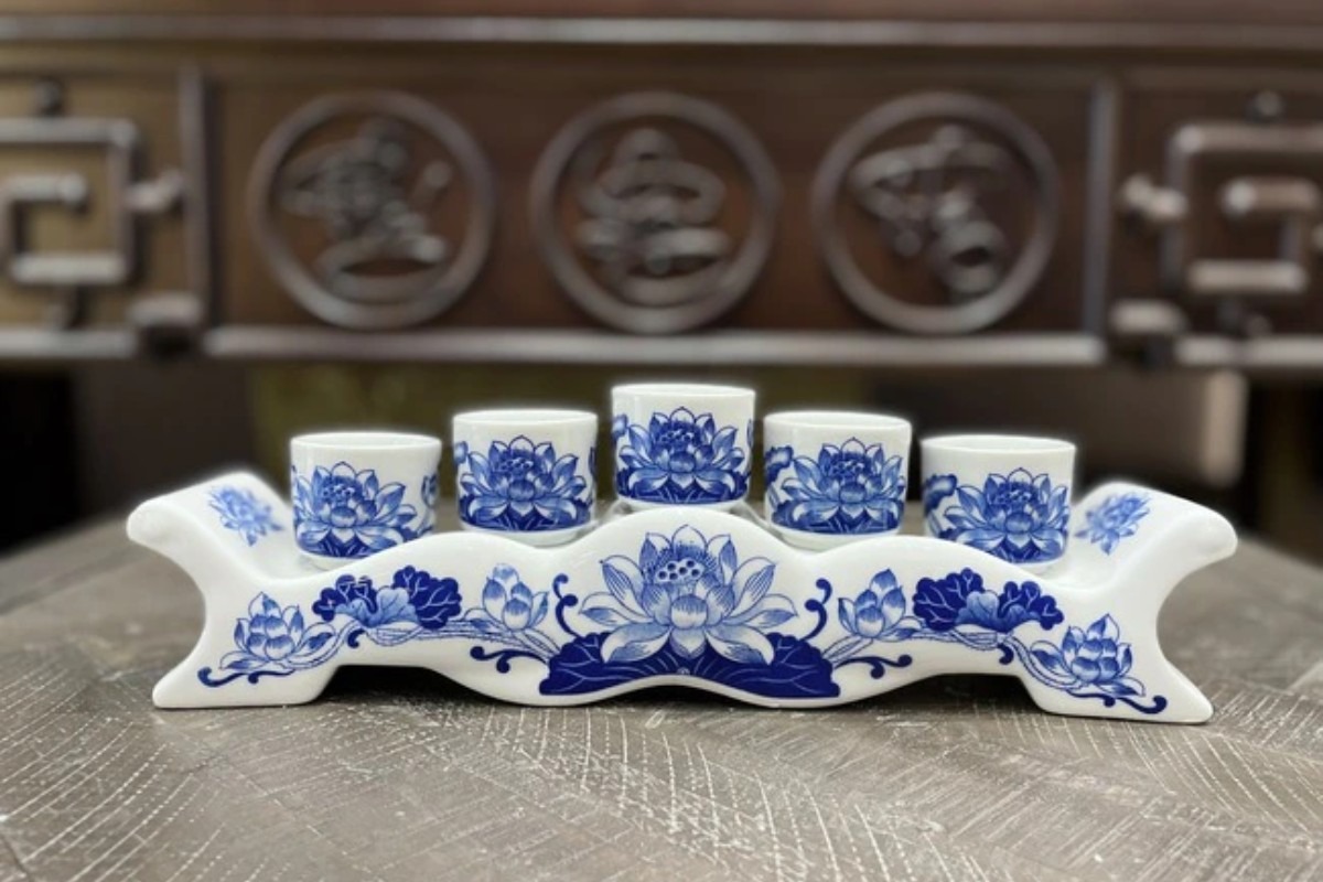 Bộ ấm trà bằng sứ trắng xanh với hoa văn sen, nổi bật trên bàn gỗ truyền thống.