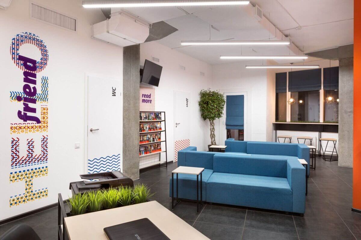 Không gian văn phòng hiện đại với sofa xanh, cây xanh và bàn làm việc tối giản.