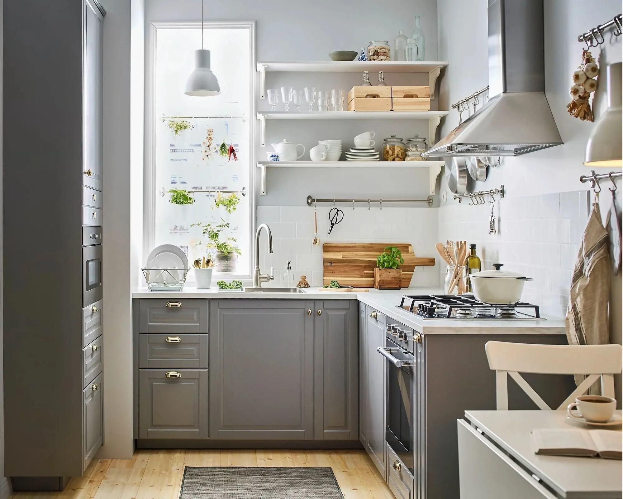 Nhà bếp hiện đại với tủ màu xám, bếp gas, kệ mở và cửa sổ sáng, trang trí cây xanh và dụng cụ nhà bếp.