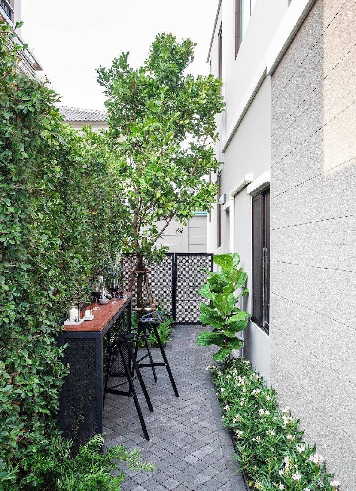 Góc sân nhỏ hiện đại đầy cây xanh với bàn ghế ngoài trời và nền gạch xám.