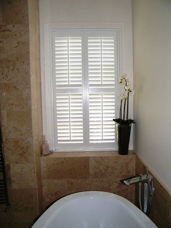 Cửa sổ chớp trắng trong phòng tắm với bồn tắm và bình hoa lan.