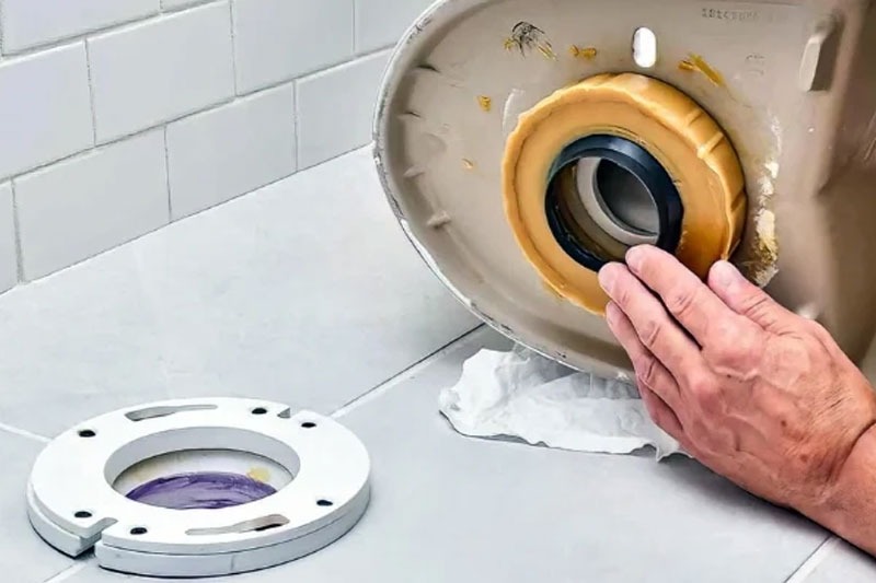 Lắp vòng đệm kín cho bồn cầu, tay người đang thao tác trên bề mặt sứ.