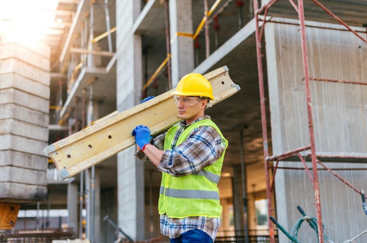 Công nhân xây dựng đội mũ bảo hộ, mặc áo phản quang, đang mang thang tại công trường xây dựng tòa nhà cao tầng.