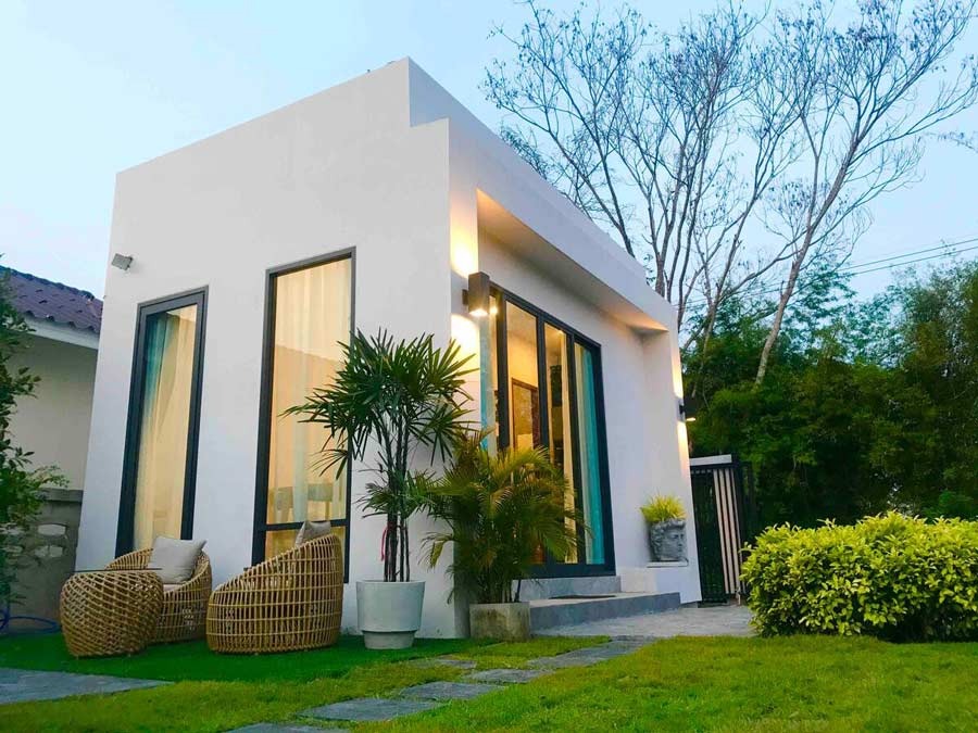 Nhà nhỏ hiện đại với sân vườn xanh tươi, cây cảnh và ghế mây ngoài trời.