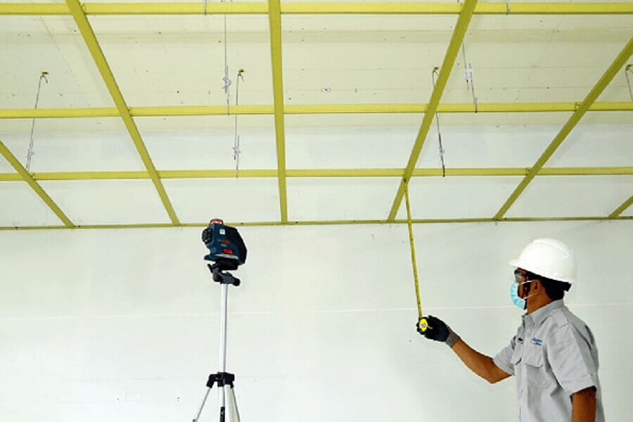 ky-thuat-lap-dat-tran-thach-cao-chim-chinh-xac-1 Kỹ sư đo đạc trần nhà bằng thước dây, thiết bị laser hỗ trợ định vị, đảm bảo độ chính xác trong xây dựng.