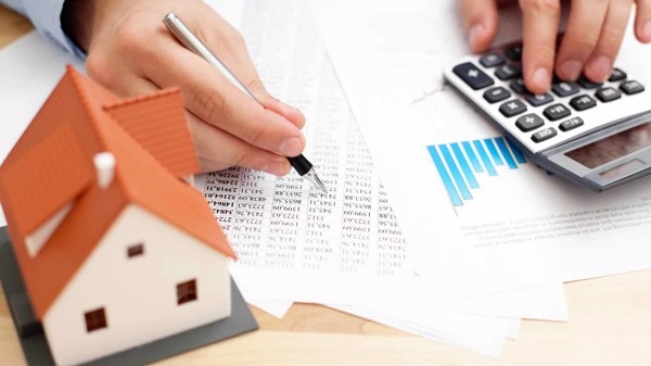 Người dùng viết trên giấy với máy tính và mô hình nhà, thể hiện khái niệm tài chính bất động sản.