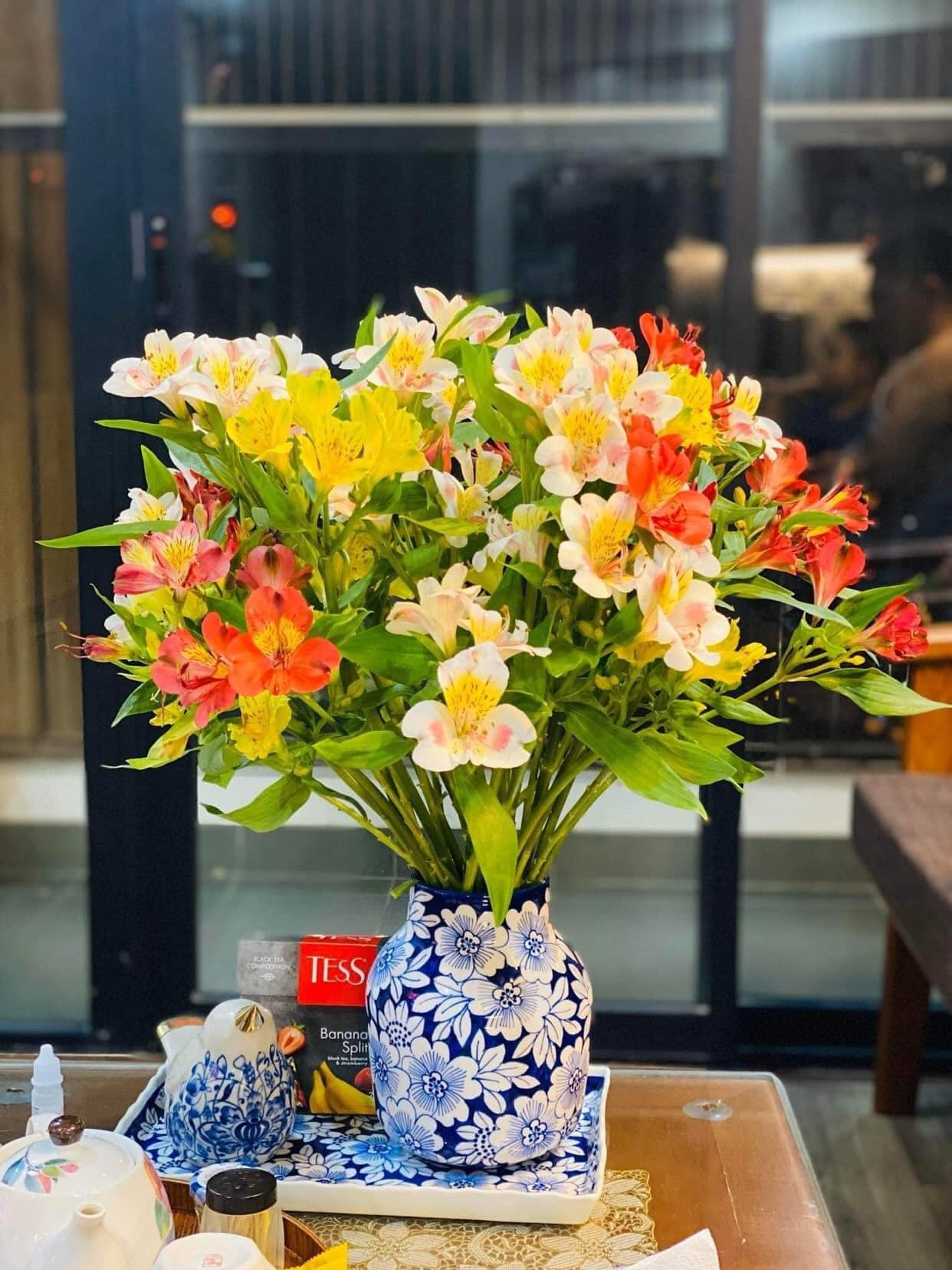 Bó hoa nhiều màu sắc trong bình gốm họa tiết xanh đặt trên bàn, mang lại vẻ đẹp tươi mới cho không gian.