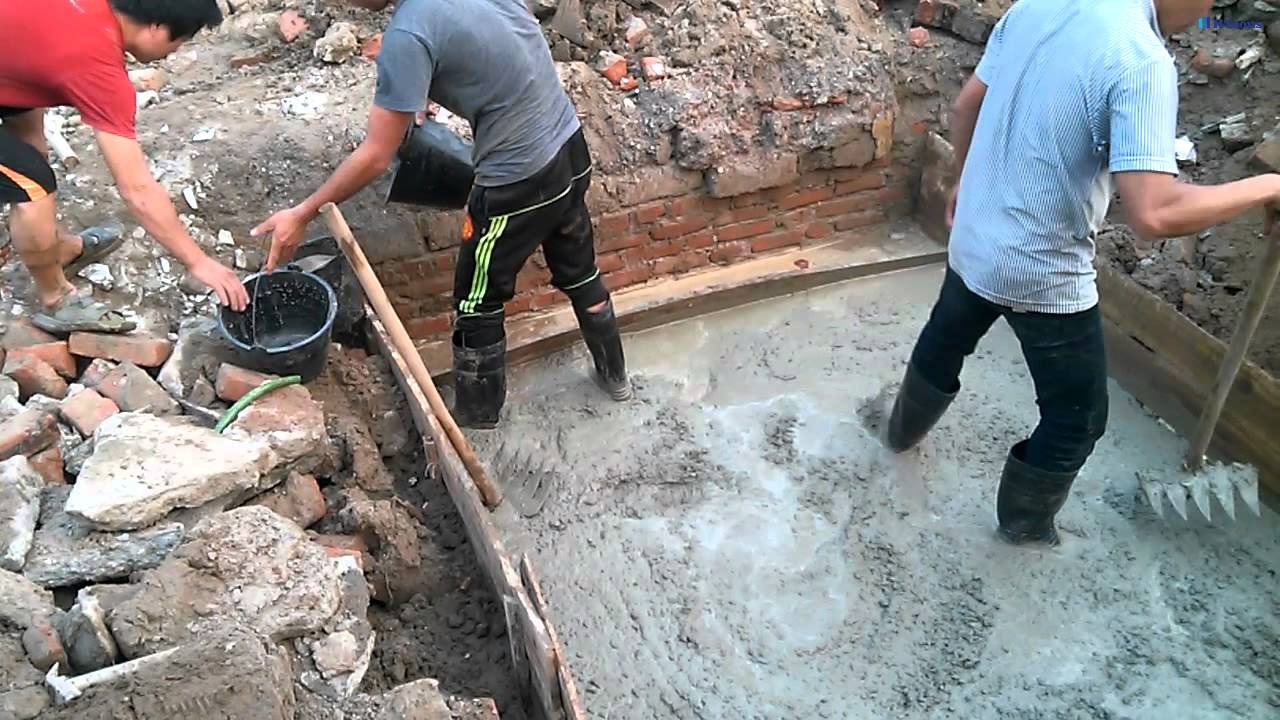 Công nhân xây dựng đang đổ bê tông cho nền móng tại công trường, sử dụng xô và dụng cụ làm phẳng.