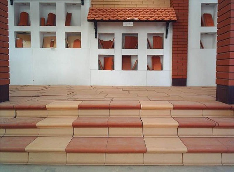 lua-chon-mau-sac-va-hoa-van-hai-hoa Cầu thang gạch lát phong cách, màu đỏ và be, bên cạnh bức tường với các kệ trưng bày.