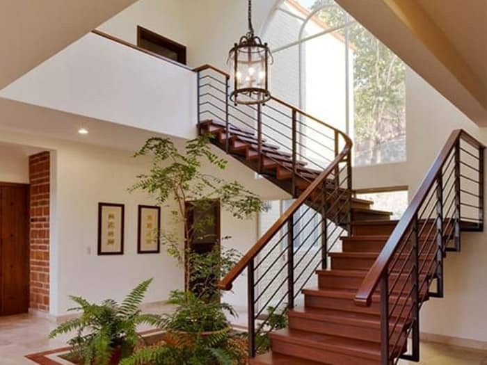 Cầu thang gỗ hiện đại với lan can kim loại trong ngôi nhà sáng sủa có cây xanh trang trí.