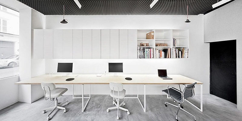 Phòng làm việc hiện đại với nội thất tối giản, ba máy tính và ghế xoay, ánh sáng tự nhiên từ cửa sổ lớn.