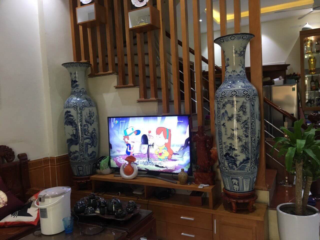 Phòng khách có tivi, hai bình gốm lớn hai bên và một bàn uống trà với bộ ấm chén.