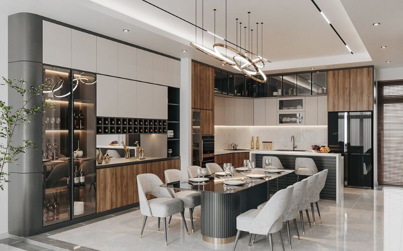 Nhà bếp hiện đại với bàn ăn sang trọng, ghế mềm màu xám, đèn treo tinh tế và tủ bếp gỗ, phong cách tối giản.