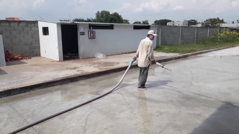 Người đàn ông đang phun nước làm sạch sân bê tông tại công trường xây dựng, một ngày nắng nhẹ.