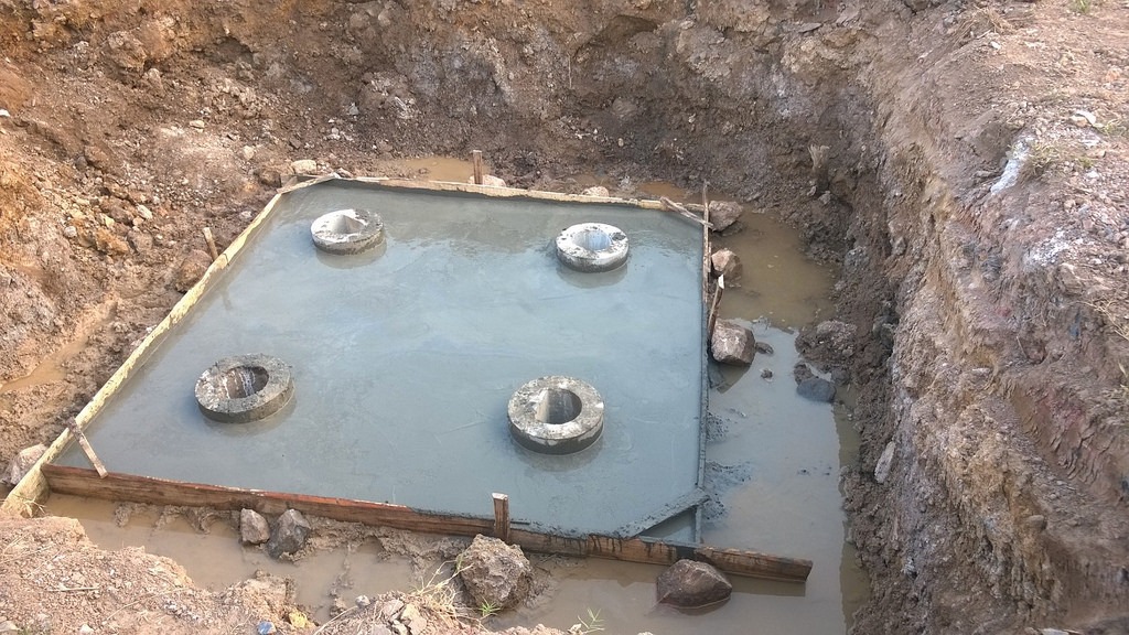 Hố móng bê tông với chốt cọc trụ trong công trình xây dựng, nền đất xung quanh sình lầy.