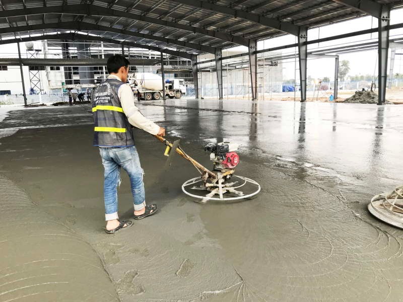 Công nhân đang sử dụng máy xoa nền bê tông trong công trường xây dựng nhà xưởng quy mô lớn.