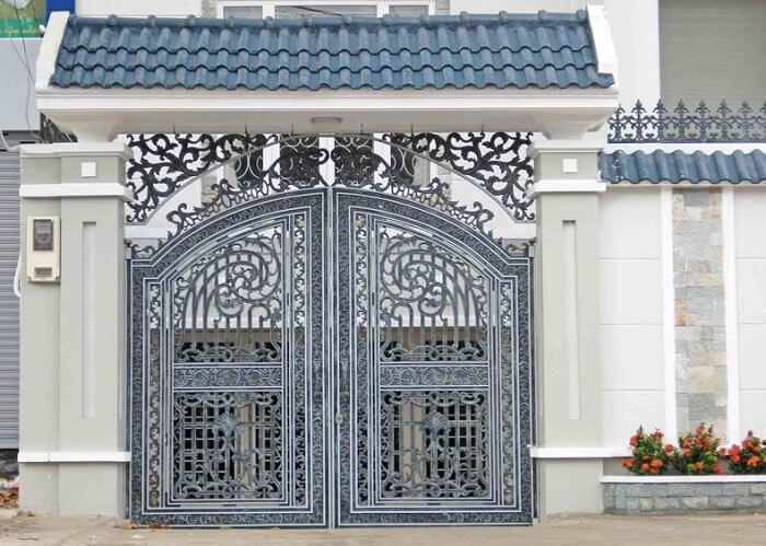 mau-cong-nha-mai-lop-ton Cổng sắt mỹ thuật với họa tiết uốn lượn, mái ngói xanh lam, trang trí tinh tế tại một công trình kiến trúc.