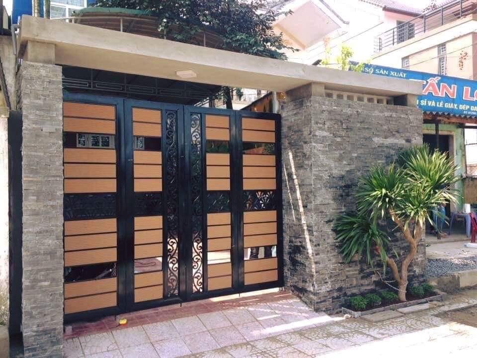 Cổng sắt màu đen và nâu sang trọng với tường đá và cây xanh, tạo không gian hiện đại và ấn tượng.