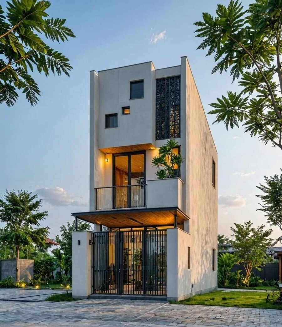 Nhà hiện đại với thiết kế tối giản, nhiều cửa sổ và ban công, bao quanh bởi cây xanh, ánh sáng vàng ấm cúng.