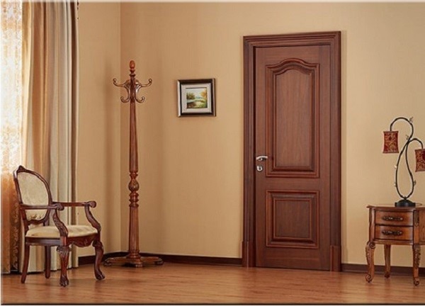 Căn phòng sang trọng với cửa gỗ, ghế tựa, móc áo, và tranh treo trên tường màu kem.