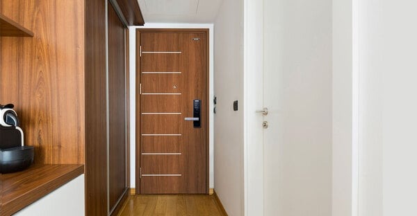 Lối vào căn hộ hiện đại với cửa gỗ sang trọng, sàn gỗ và tủ gỗ tối màu bên trái, tường trắng.