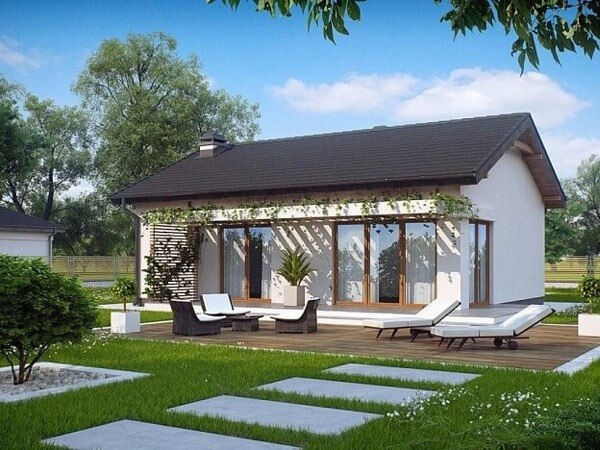 Nhà cấp bốn hiện đại với sân vườn xanh mát và ghế thư giãn trên sàn gỗ, bao quanh bởi cây cối.