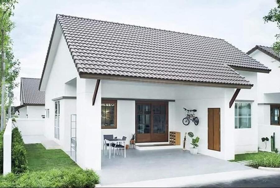 Nhà cấp 4 hiện đại, mái ngói nâu, sân rộng với bàn ghế và cây xanh, xe đạp treo tường.