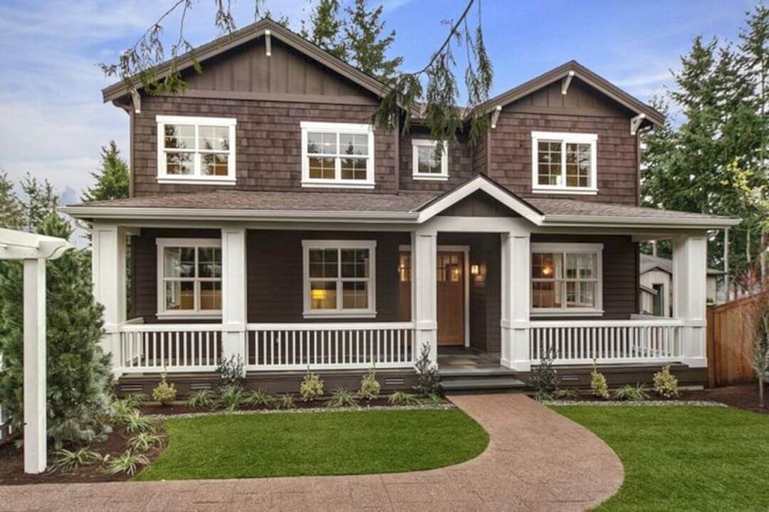 Ngôi nhà hai tầng màu nâu với hành lang rộng, sân vườn xanh mướt và cây cối xung quanh.