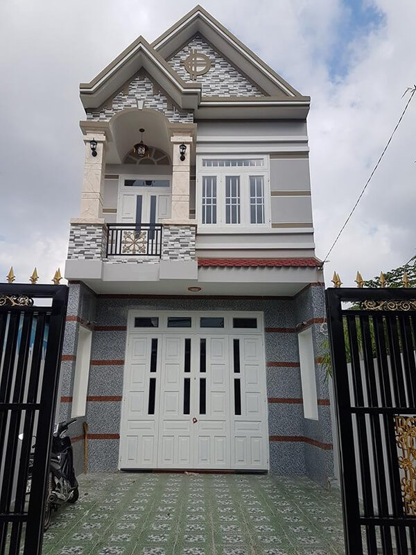 Ngôi nhà hiện đại hai tầng với cổng sắt, cửa trắng và kiến trúc mái độc đáo, trời quang đãng.
