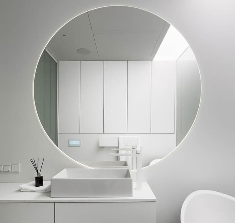 Phòng tắm hiện đại với bồn rửa mặt trắng và gương lớn hình tròn. Thiết kế tối giản, ánh sáng tự nhiên dịu nhẹ.