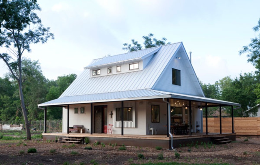 Ngôi nhà nhỏ kiểu nông thôn với mái kim loại, sân hiên rộng và cây xanh xung quanh.